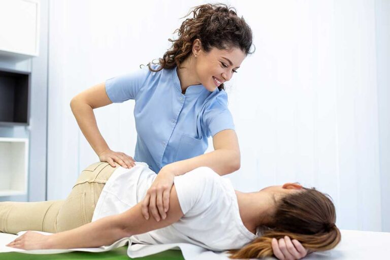 A chiropractor assesses an athlete’s back while the athlete stretches on a padded table.
